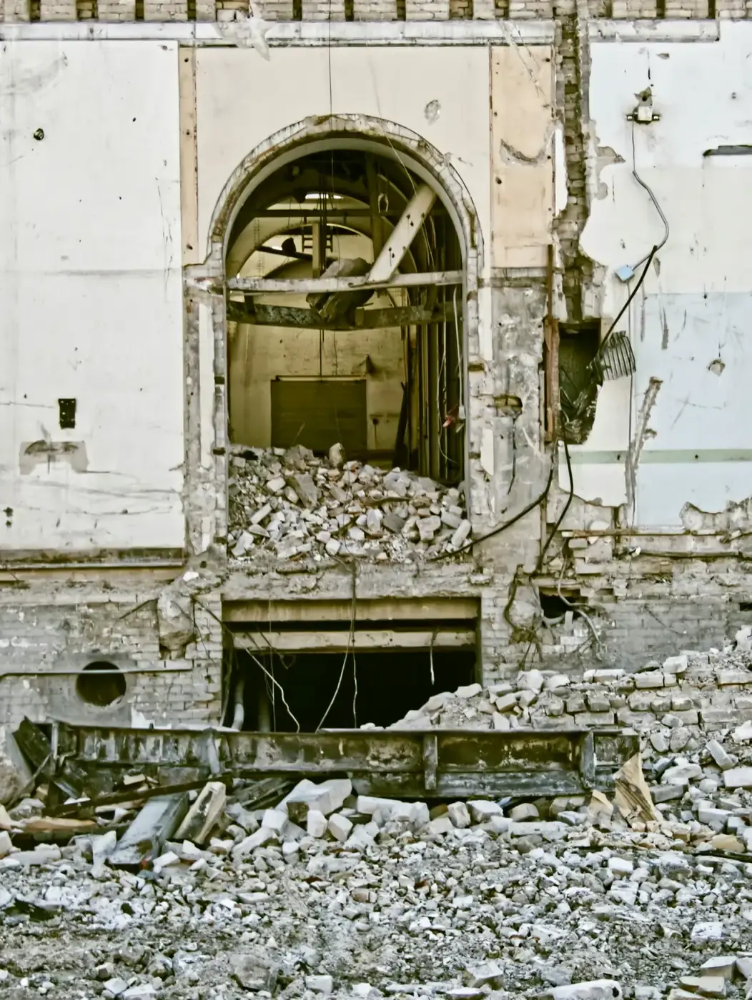 An arched opening left in a masonry wall, with rubble on the floor below it