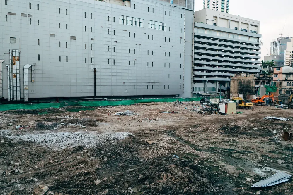 A cleared and levelled site of bare mud with city buildings standing behind it