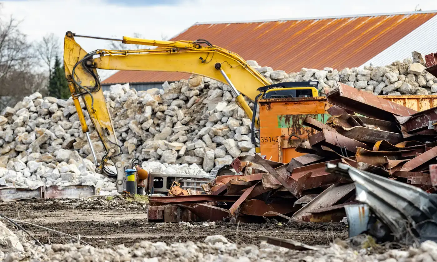 An excavator beside a stockpile of broken concrete, with a skip of separated scrap steel