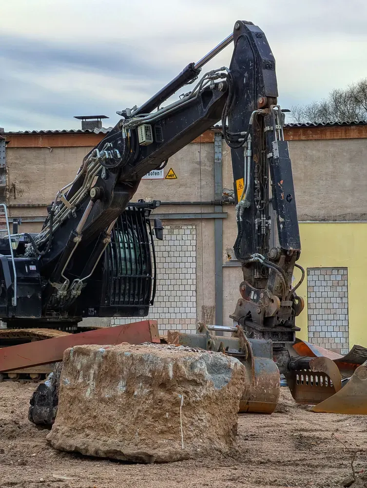 An excavator standing beside a large block of broken concrete in an industrial yard