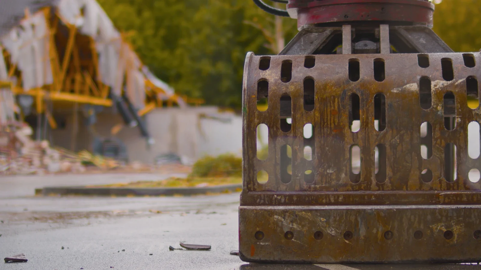 A close view of a grapple attachment on a demolition site, the works out of focus behind
