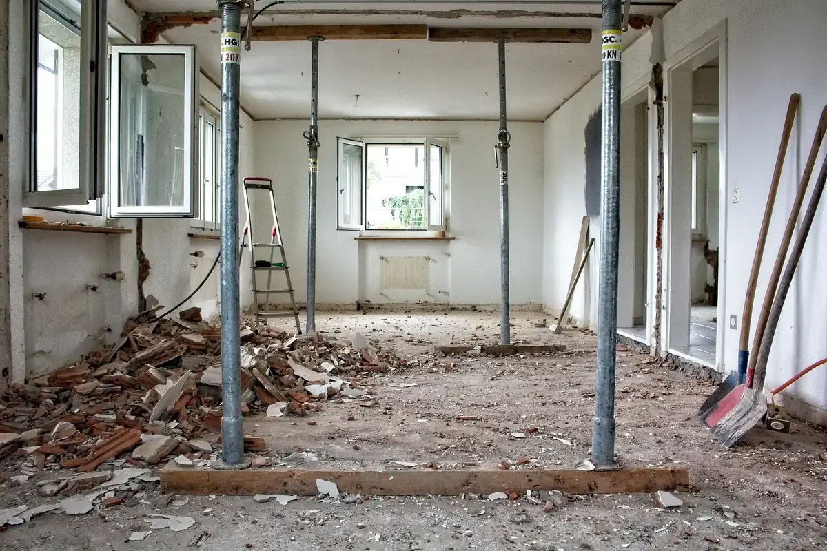 Steel props holding a ceiling inside a stripped room, rubble and shovels on the floor