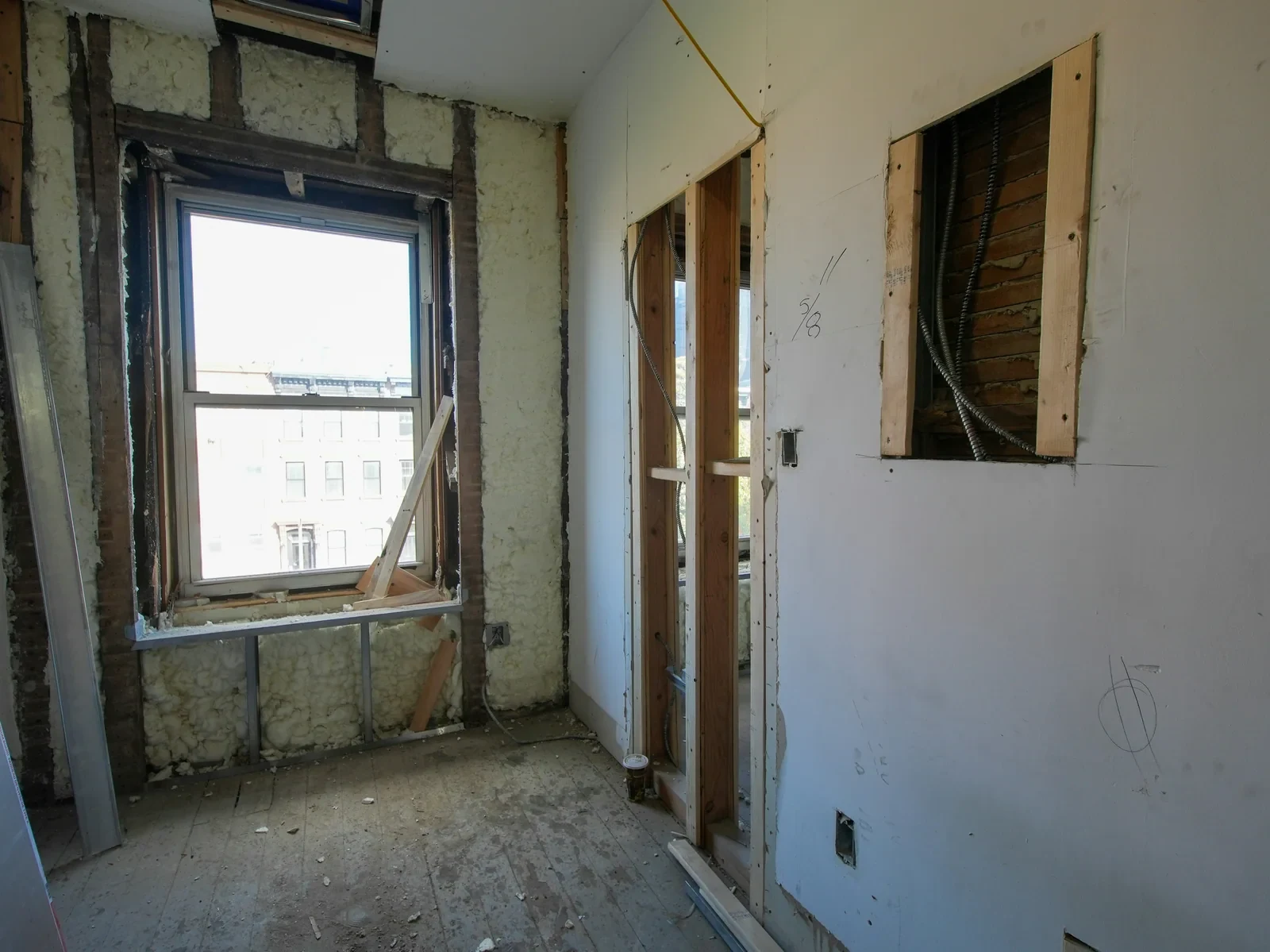 An interior stripped back to studs and insulation, daylight coming through the window opening