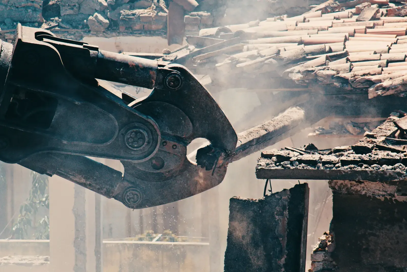 Hydraulic shear jaws closing on a timber beam, dust drifting through the frame