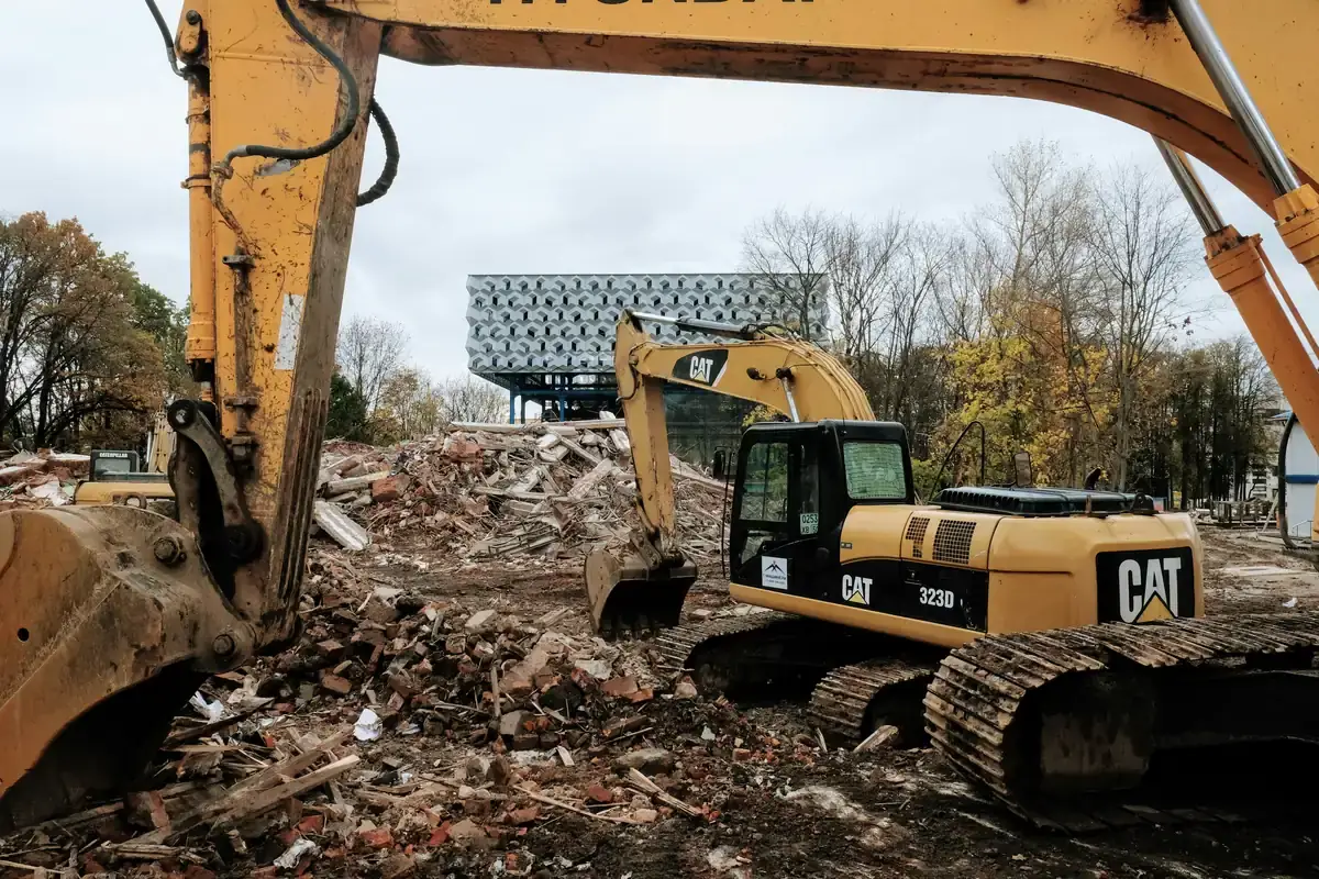 Two excavators working across a cleared site strewn with brick rubble